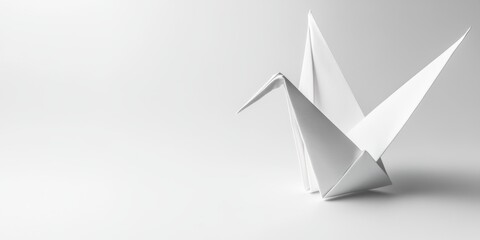 Obraz premium A lone paper crane made from white origami paper, sitting on a stark white surface with a gentle shadow. 