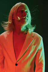 Stylish man with long hair in a modern suit against a colorful gradient background, showcasing contemporary fashion and artistic expression in vibrant hues