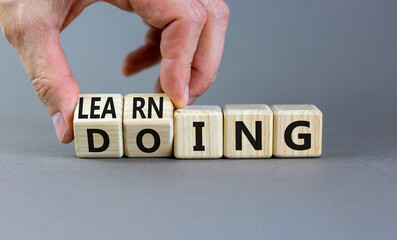 Doing or learning symbol. Businessman turns wooden cubes and changes the word Doing to Learning ....