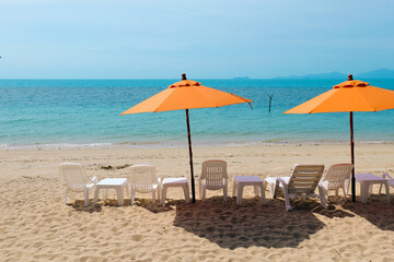 Relaxing beach scene with orange umbrellas and lounge chairs by the tranquil sea.
