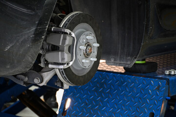 Close-up of a car brake system on a maintenance lift in an auto repair shop.