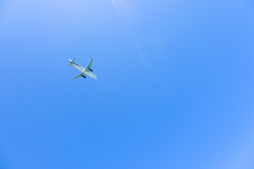 A green airplane flying high in a clear blue sky on a sunny day.