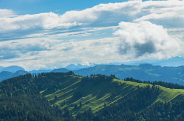 Expansive mountain landscape with green hills and dramatic cloud formations under a bright blue sky