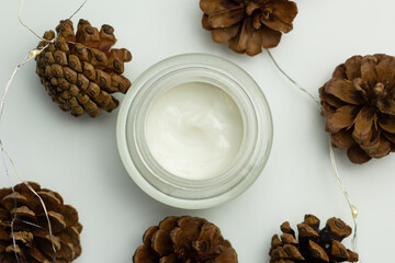 Concept of winter skincare. Close-up of a jar of moisturising cream and pine cones.