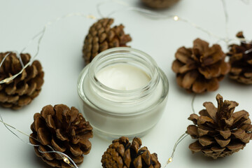 Concept of winter skincare. Close-up of a jar of moisturising cream and pine cones.