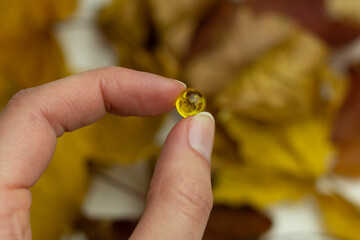 Concept of autumn supplementation. Closeup of a vitamin D capsule and yellow leaves.