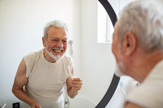 Senior man brushing teeth in bathroom mirror