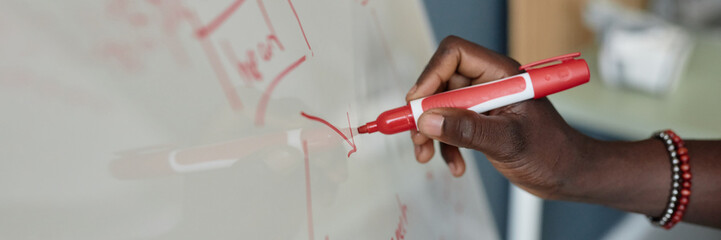 Close-up view of hand holding red marker and writing on whiteboard during a presentation in...