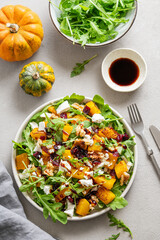 Autumn salad with pumpkin, arugula, feta cheese, nuts and dried berries in a plate on a light background