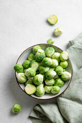 Fresh brussels sprouts in a bowl on a light gray background with green napkin. Vegetarian healthy food concept.