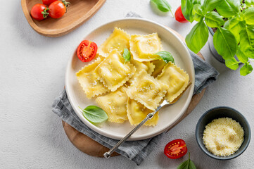 Ravioli pasta with parmesan, tomatoes and basil in a plate on a napkin and wooden board on a light  background