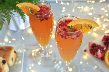 Pomegranate Mimosas for a festive brunch - a glass containing a mimosa garnished with pomegranate seeds, an orange slice and thyme