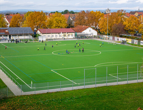 Soccer players practice on a vibrant field surrounded by autumn foliage in a small town