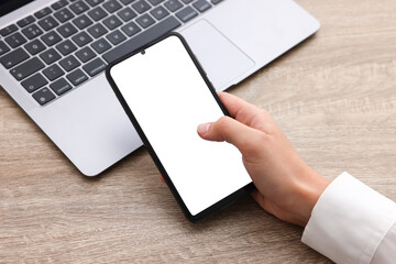 Woman unlocking smartphone with fingerprint scanner near laptop at wooden table, closeup