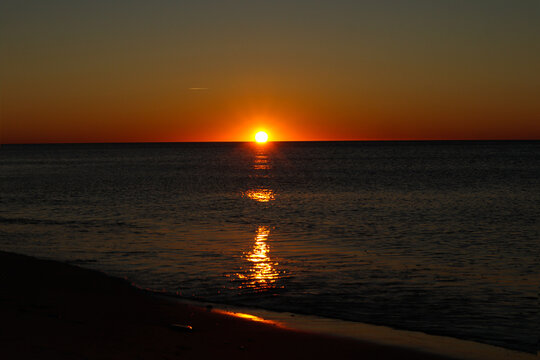 The orange sun sets on the edge of the sea