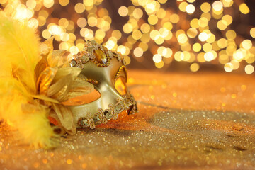 Beautiful carnival mask on golden shiny background, space for text. Bokeh effect
