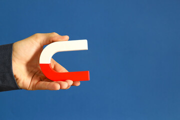 Man holding horseshoe magnet on blue background, closeup. Space for text