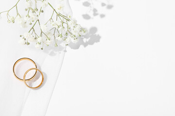 Golden wedding rings, veil and flowers on white background, top view. Space for text