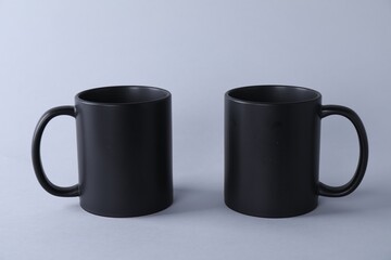 Two blank black mugs on light background. Mockup for design