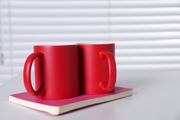Blank red ceramic mugs and notebook on white table. Mockup for design