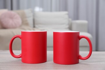 Blank red ceramic mugs on white wooden table. Mockup for design