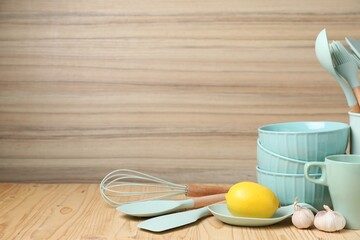Dishware, cooking utensils, lemon and garlic on wooden table. Space for text