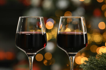 Red wine in glasses against blurred Christmas lights, closeup. Bokeh effect