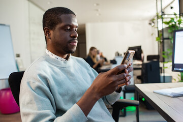 Young black businessman using smartphone at office computer desk