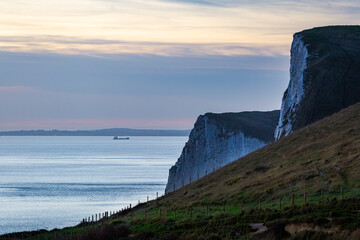Cliffs along the bay at Durdle door during sunset with a lone ship in the distant