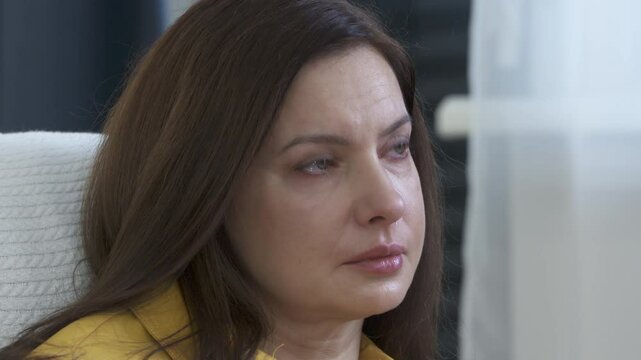 Adult 44 year old woman sitting on sofa in living room in front of TV watching melodrama. Impressionable woman cries wiping tears worried while watching movie.