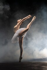 Graceful ballet dancer performing an elegant leap in a misty theater setting