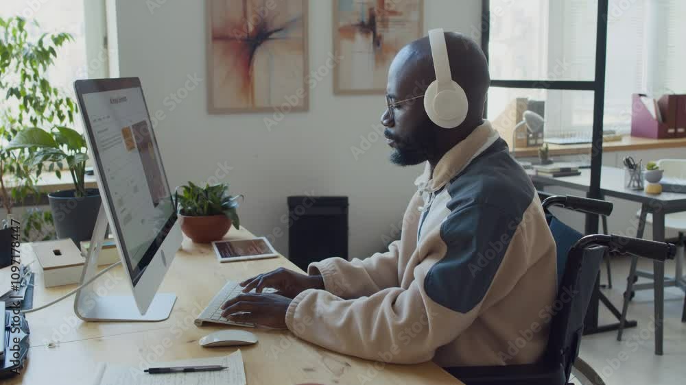 Wall mural medium side shot of black male software developer with disability, using wheelchair, sitting at desk