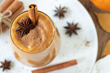 Pumpkin smoothie with cinnamon stick and star anise on wooden table with autumn leaves. Top view....