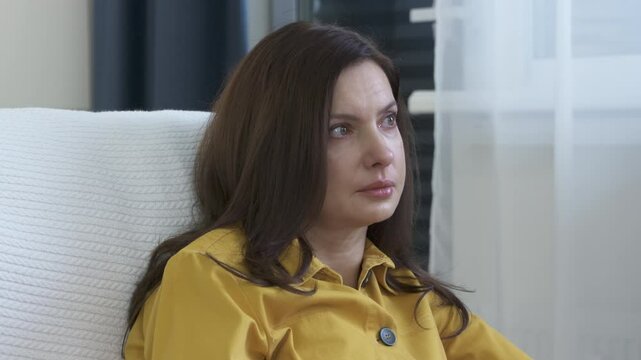 Adult 44 year old woman sitting on sofa in living room in front of TV watching melodrama. Impressionable woman cries wiping tears worried while watching movie.