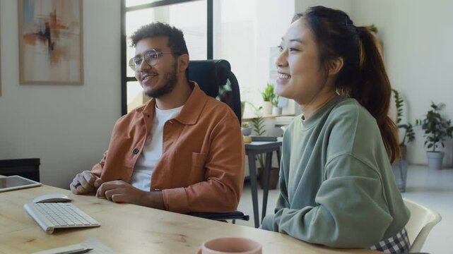 Medium slowmo shot of cheerful Chinese female and Middle Eastern male programmers testing new software after completing team project, then giving high fives on successful program execution
