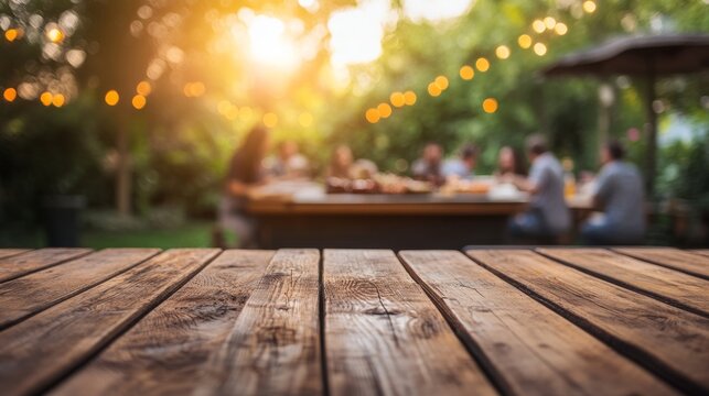 Empty wooden table and blurred view of a group of people having BBQ barbecue outdoors. Wood desk in front of a natural garden background