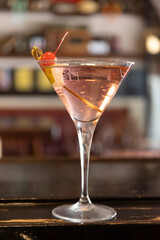 Close up shot of a Manhattan Cocktail on the counter of an aperitif bar in Milan, Italy. Red sweet cherry on a stick, on the edge of the glass. Aperitif, drinking.