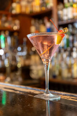 Close up shot of a Manhattan Cocktail on the counter of an aperitif bar in Milan, Italy. Red sweet cherry on a stick, on the edge of the glass. Aperitif, drinking.