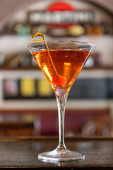 Close up shot of a Manhattan Cocktail on the counter of an aperitif bar in Milan, Italy. Red sweet cherry on a stick, on the edge of the glass. Aperitif, drinking.