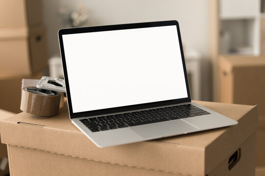 Close up shot of laptop computer with white blank display placed on cardboard box in e-commerce storage room. PC screen with copy space for shipping, logistic application interface, business app