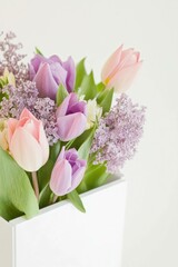 Beautiful bouquet of pink and purple tulips combined with lilac flowers in a white vase, adding elegance and freshness to any interior space.