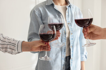People clinking glasses of red wine indoors, closeup