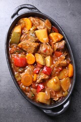 Delicious stew with vegetables in baking dish on grey table, top view