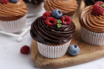 Tasty cupcakes with chocolate cream and berries on white marble table, closeup