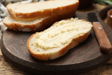 Fresh bread with butter and knife on wooden table, closeup