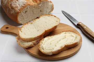 Fresh bread with butter and knife on white tiled table, closeup