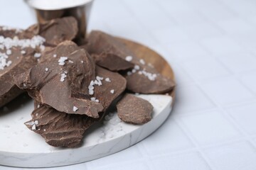Pieces of tasty chocolate with salt on white tiled table, closeup. Space for text