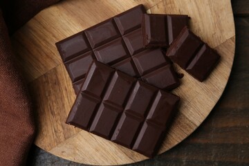 Pieces of delicious dark chocolate bar on wooden table, flat lay