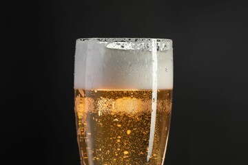Glass of beer with condensation drops on black background, closeup