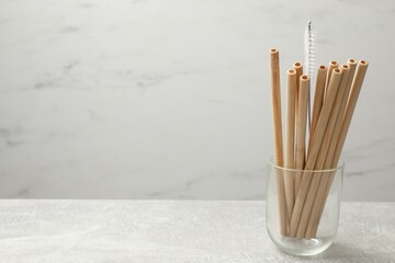 Bamboo drinking straws and cleaning brush in glass on light table, space for text